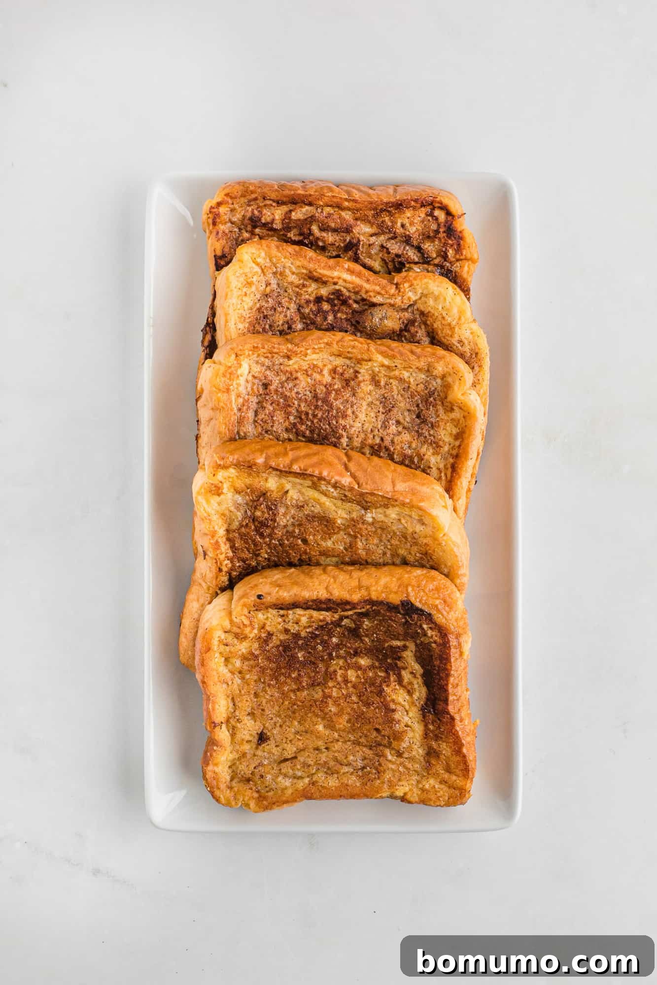 A row of cooked French toast slices lined up on a plate.