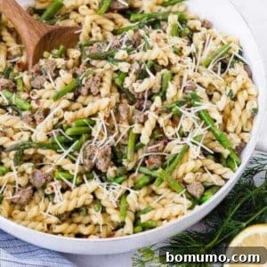 Image of lemon pasta in a white skillet with a wooden spoon. Garnished with lemon and dill.