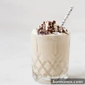 A glass of whiskey milkshake topped with whipped cream and chocolate syrup, served with a striped straw.