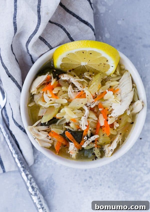 A close-up, overhead view of lemon chicken orzo soup in a white serving bowl, generously sprinkled with fresh black pepper, highlighting its rich texture and inviting steam.