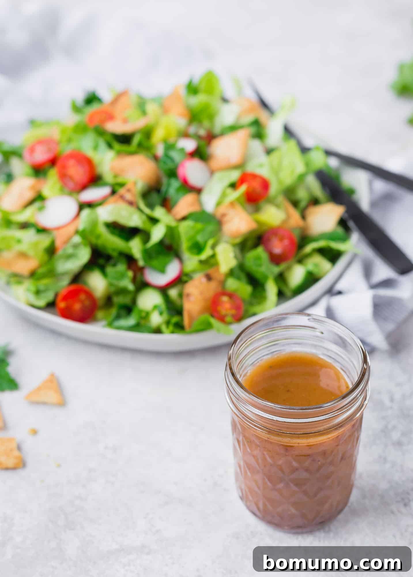 Fattoush salad in a large bowl, with a glass jar of homemade dressing prominently displayed in the foreground of the photo, indicating its central role in the dish.