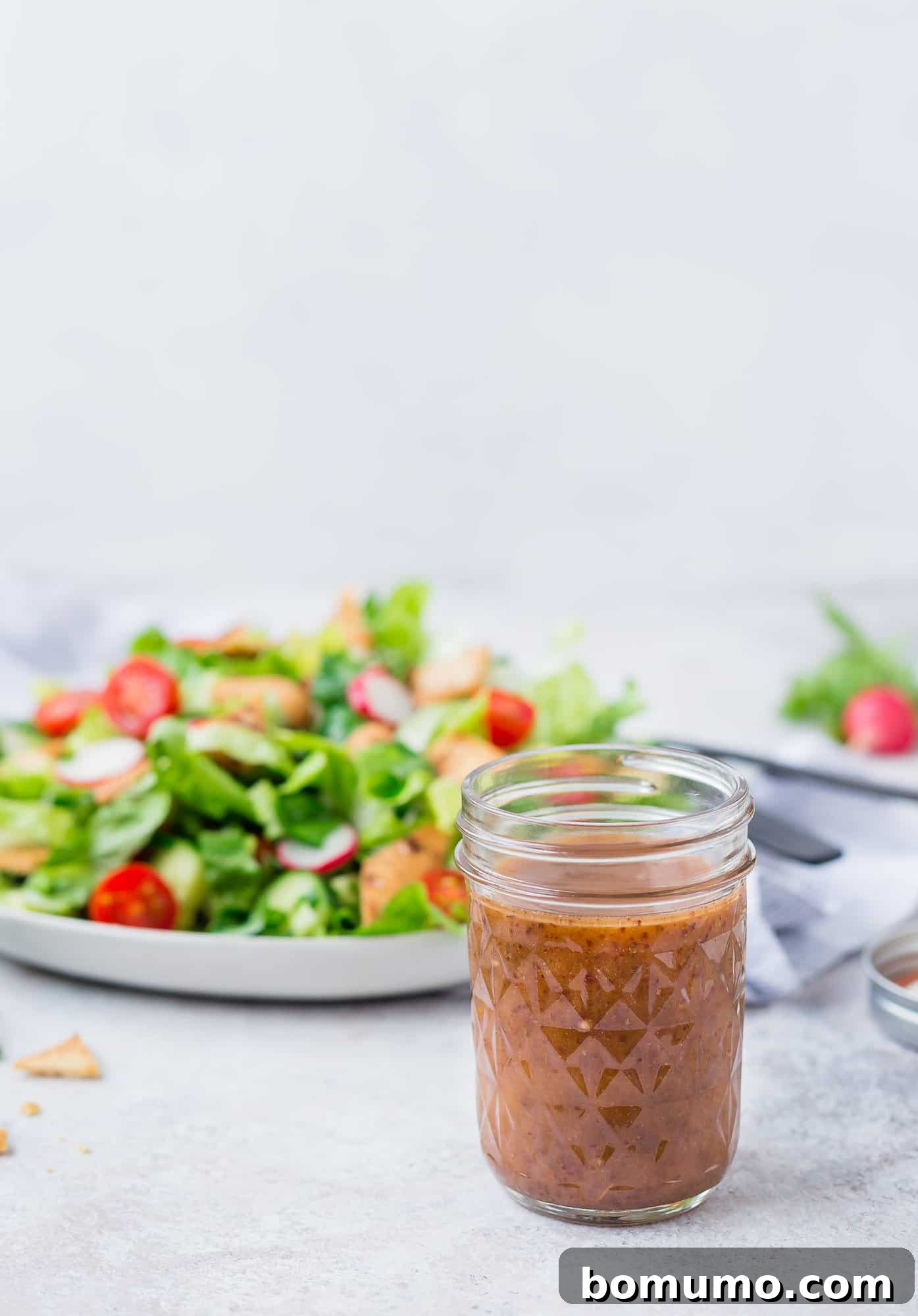 A clear glass jar filled with a rich, amber-colored Fattoush salad dressing, showcasing its vibrant ingredients and smooth consistency, ready to be poured over a fresh salad.