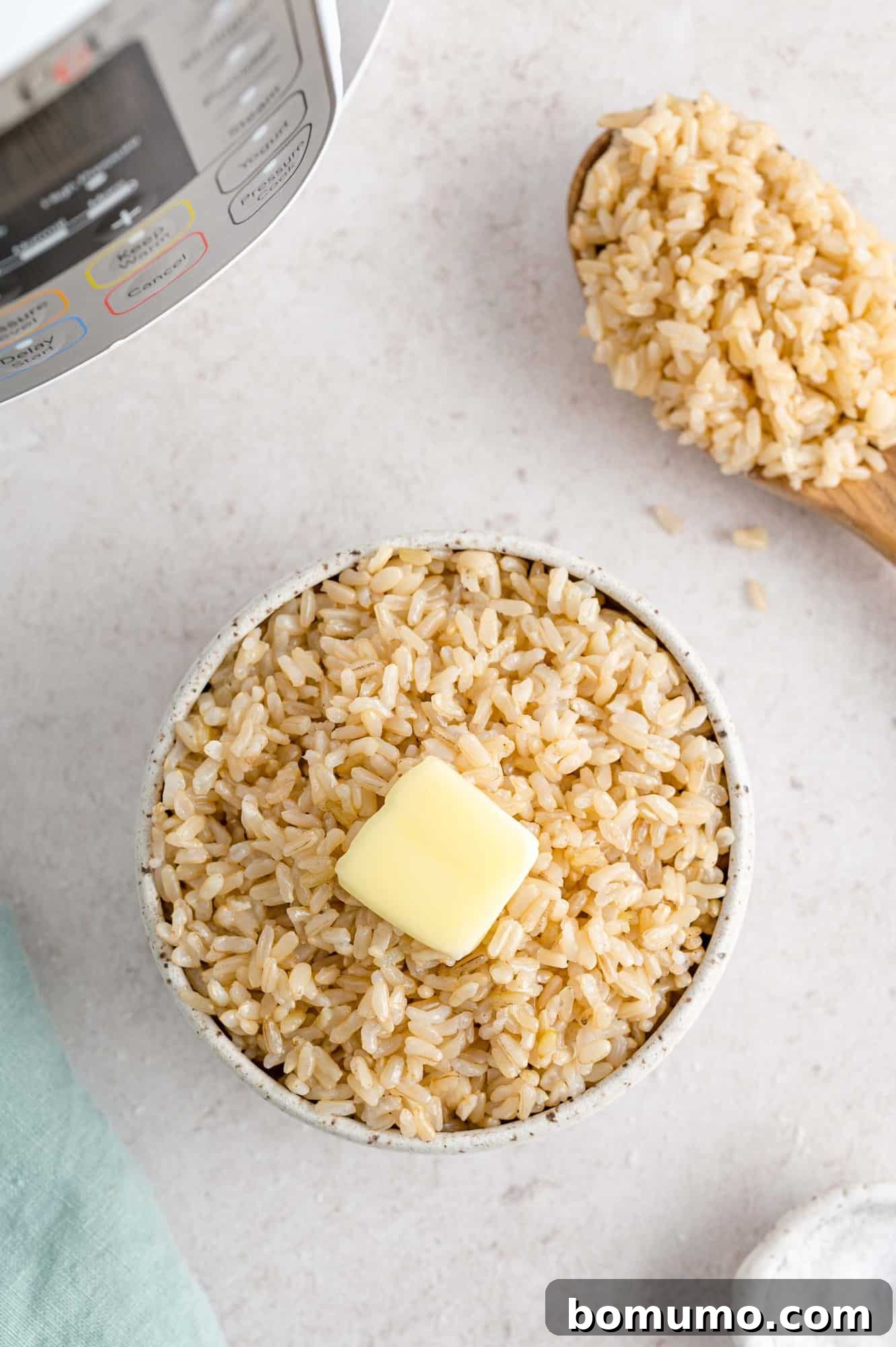 Fluffy brown rice in a white bowl with a pat of butter, an Instant Pot visible in the soft-focus background.