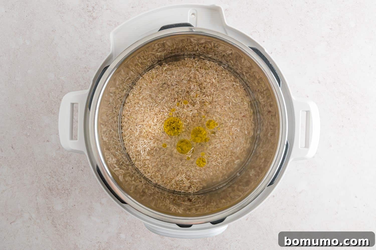 Uncooked brown rice, water, and oil neatly arranged in the Instant Pot's inner pot, ready for cooking.