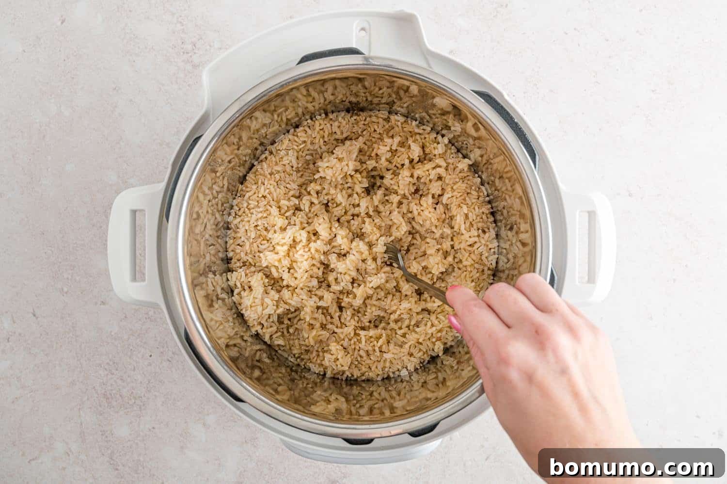 Fluffy brown rice being gently fluffed with a fork inside the Instant Pot after cooking, showing perfect texture.
