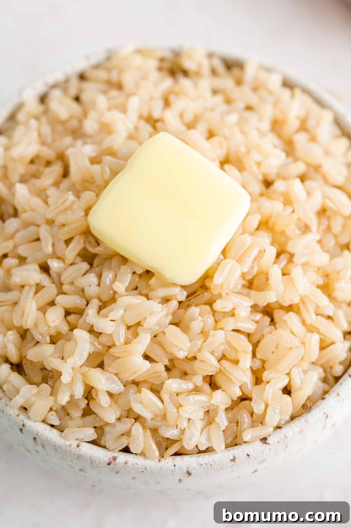 Close-up view of perfectly cooked brown rice with a pat of melting butter in a simple white bowl, ready to enjoy.