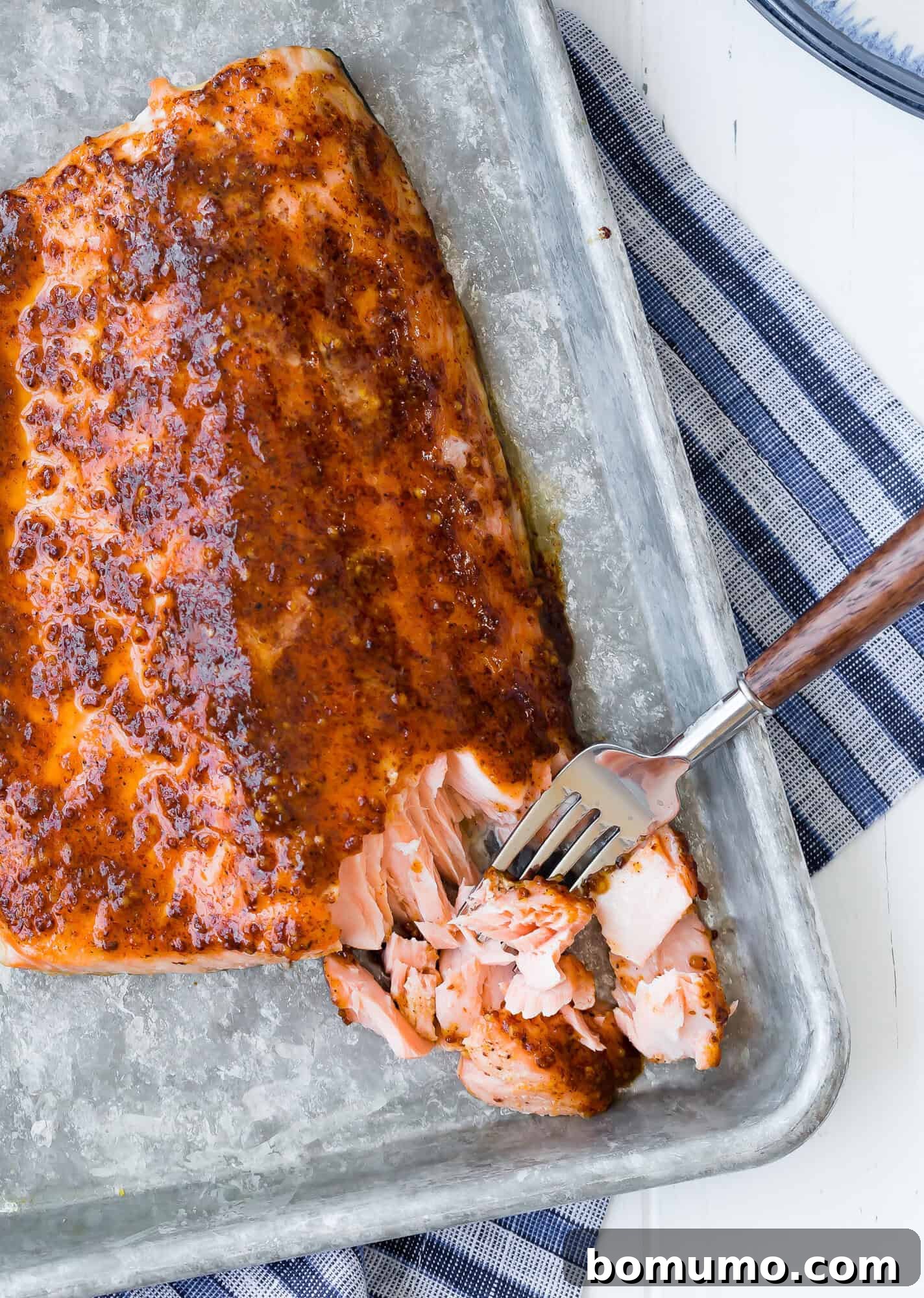 Maple mustard glazed baked salmon being flaked with a fork, showcasing its tender texture and caramelized glaze.