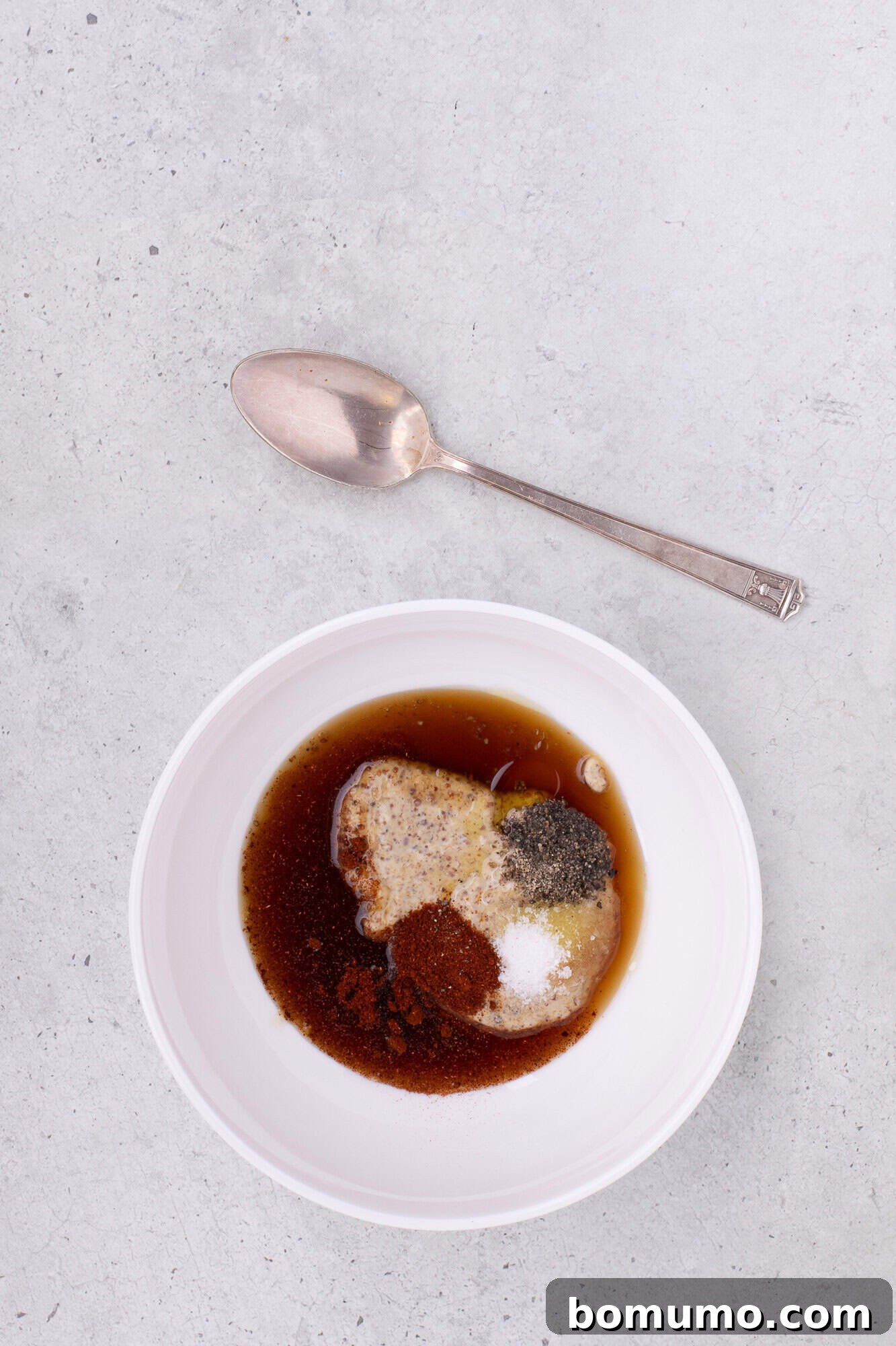 Glaze ingredients, including mustard, maple syrup, and spices, unmixed in a small white bowl.