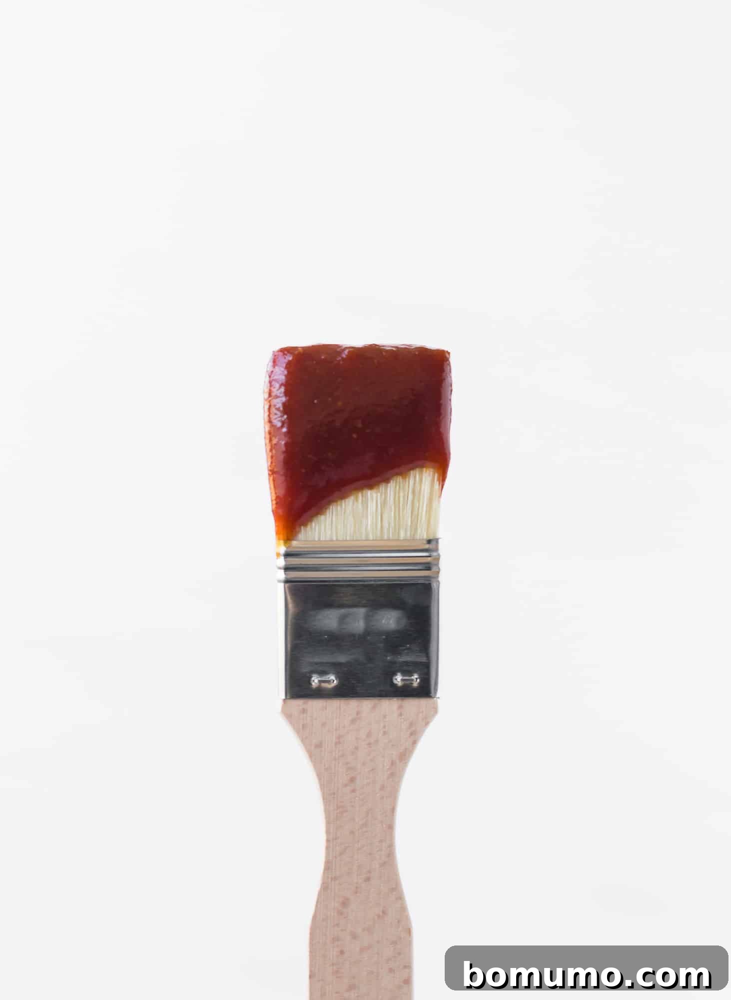 Thick BBQ sauce coating a wooden handled basting brush.