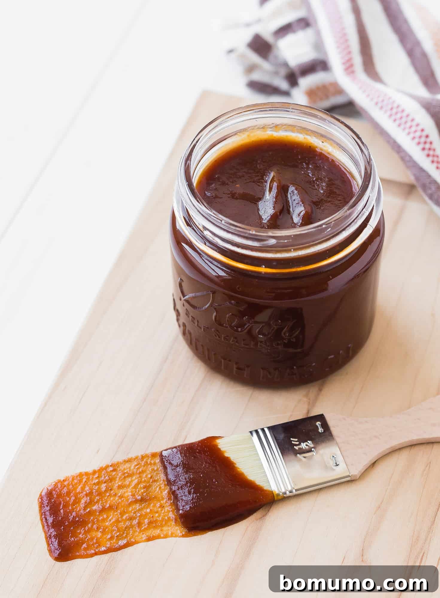Barbecue sauce in a small glass jar and on a wooden handled brush, ready for grilling.