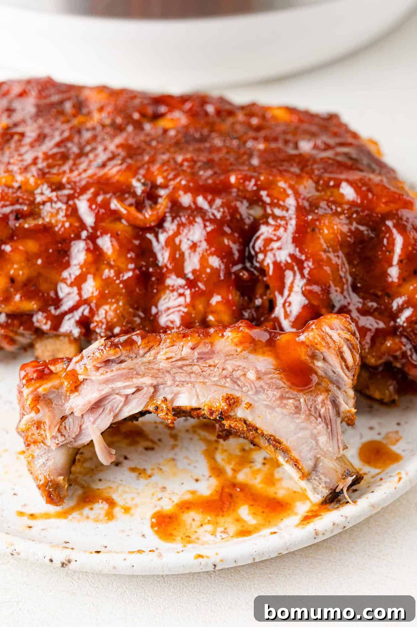 These Instant Pot ribs give you fall-off-the-bone, flavorful ribs, in around an hour! It's almost magical and it's going to be your go-to when you want ribs but don't have hours to spare. Instant Pot ribs with barbecue sauce, cut to show juicy interior.