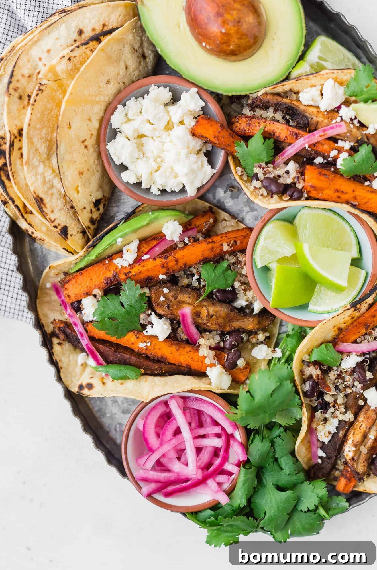 The most flavorful vegan tacos with roasted carrots, mushrooms, and lots of protein thanks to quinoa and black beans. Add cheese if you're not vegan! Carrot and mushroom tacos beautifully arranged on a tray with fresh toppings, ready to be enjoyed.