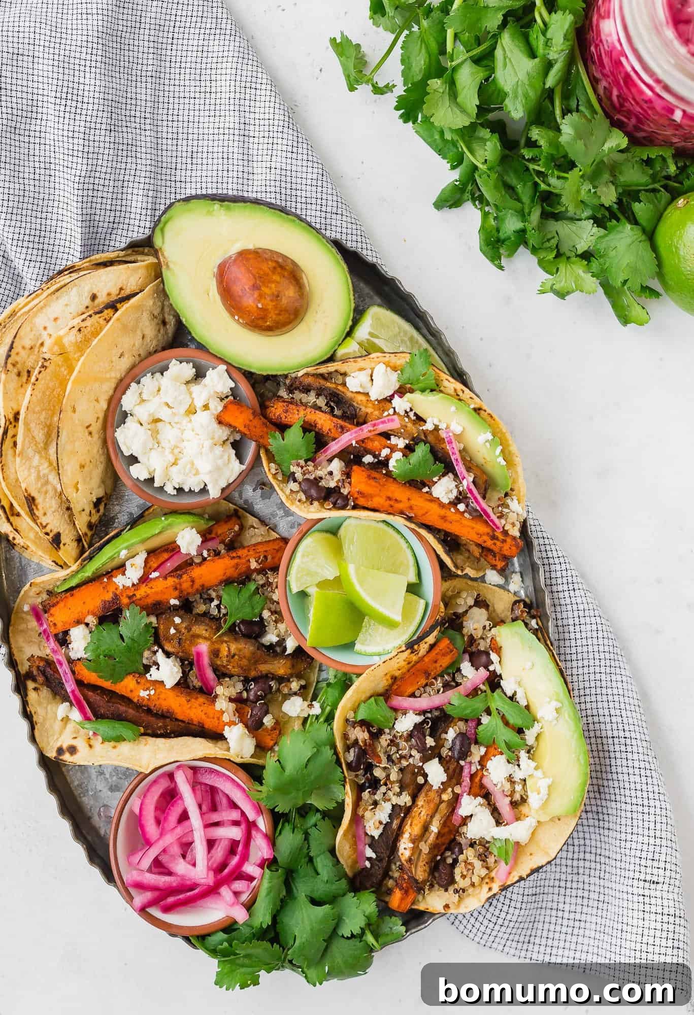 Plant Powered Roasted Tacos 2 A vibrant spread of tacos on a tray, accompanied by bowls of colorful toppings like pickled red onions, crumbled cheese, and fresh lime wedges.