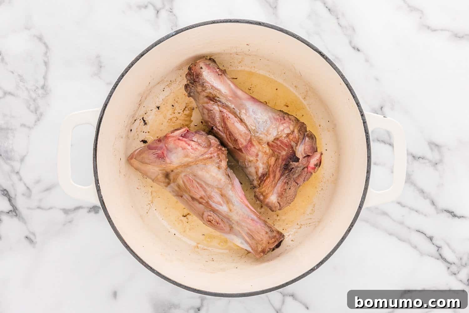 Raw lamb shanks achieving a perfect golden-brown sear in a hot Dutch oven, a crucial step for locking in flavor.