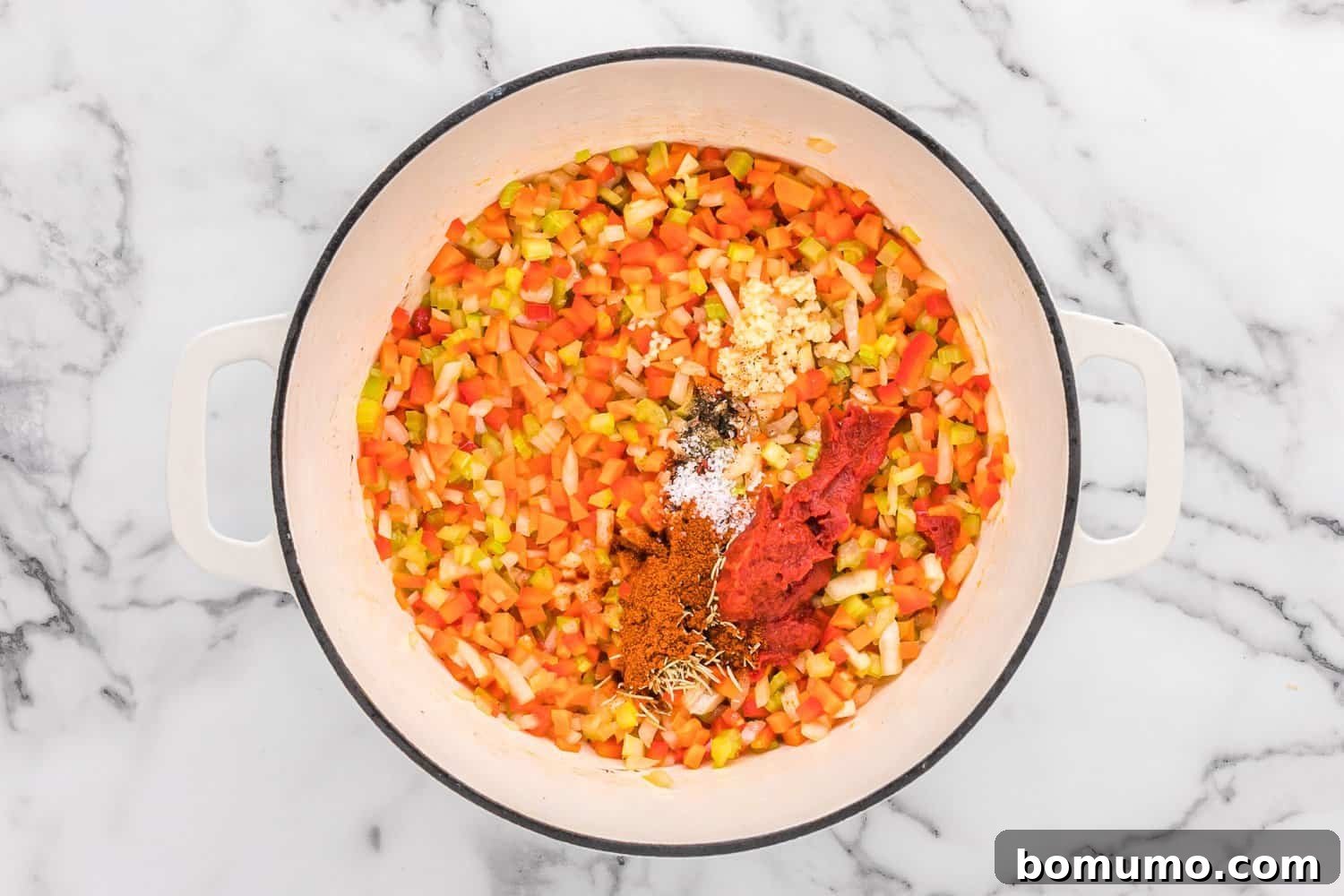 A colorful medley of finely diced carrots, celery, onions, and bell peppers sautéing in a Dutch oven, forming the aromatic base for a rich sauce.