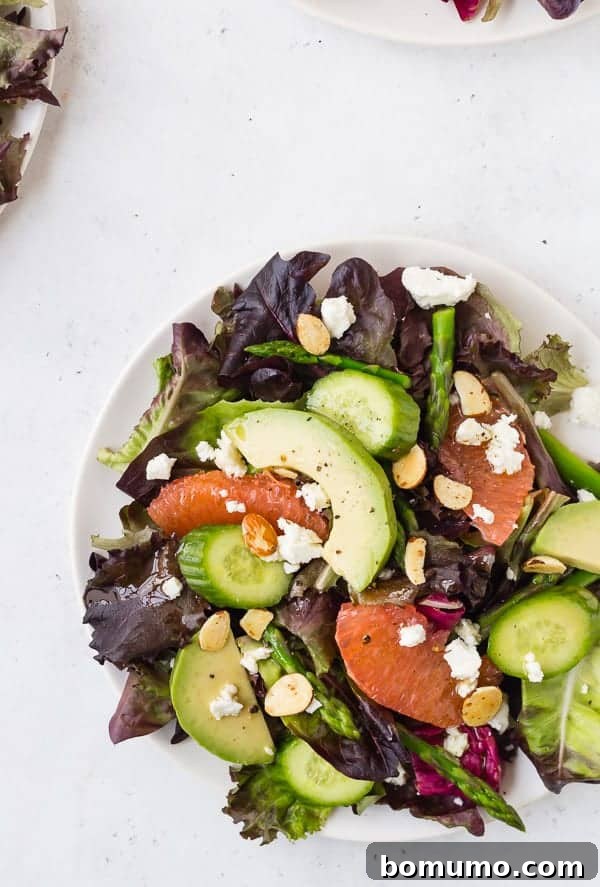Overhead view of a beautifully composed spring salad on a white plate, showcasing the vibrant colors of grapefruit, asparagus, and avocado.