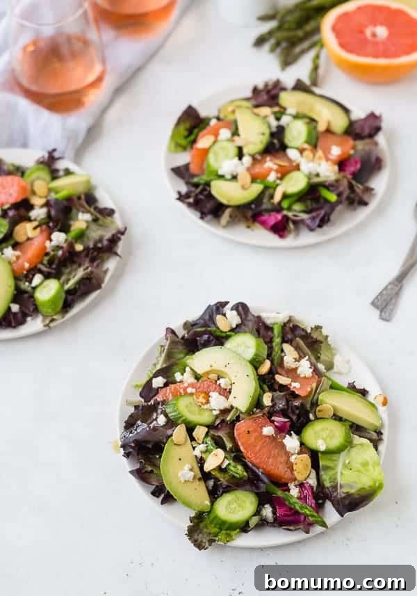Multiple servings of Spring Salad with Rosé Vinaigrette beautifully arranged on white plates, accompanied by wine glasses, perfect for a gathering.