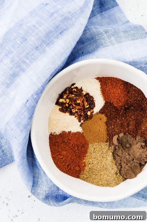 A white bowl filled with a vibrant homemade chili seasoning blend, featuring various spices with a blue towel in the background.