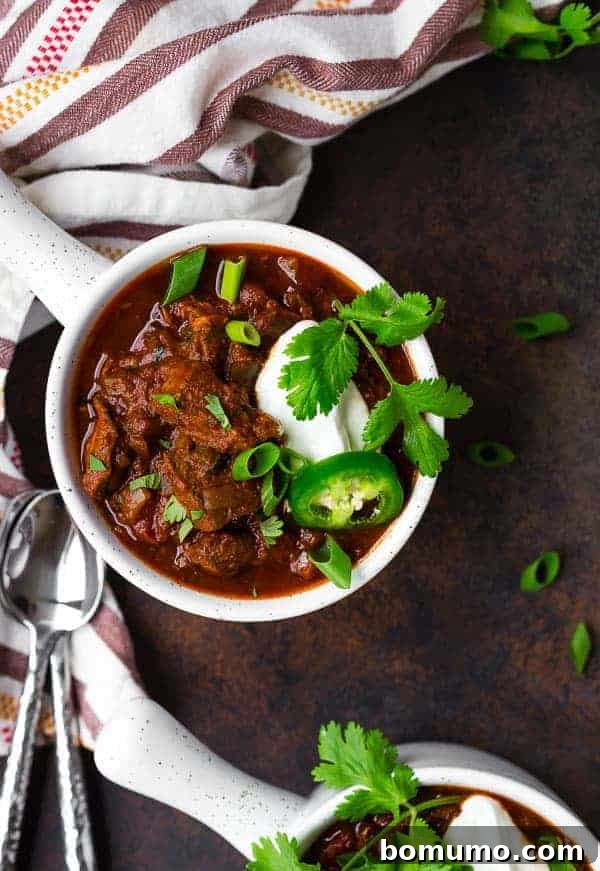 Image of Texas chili in a white bowl, garnished with sour cream, cilantro, and jalapeno.