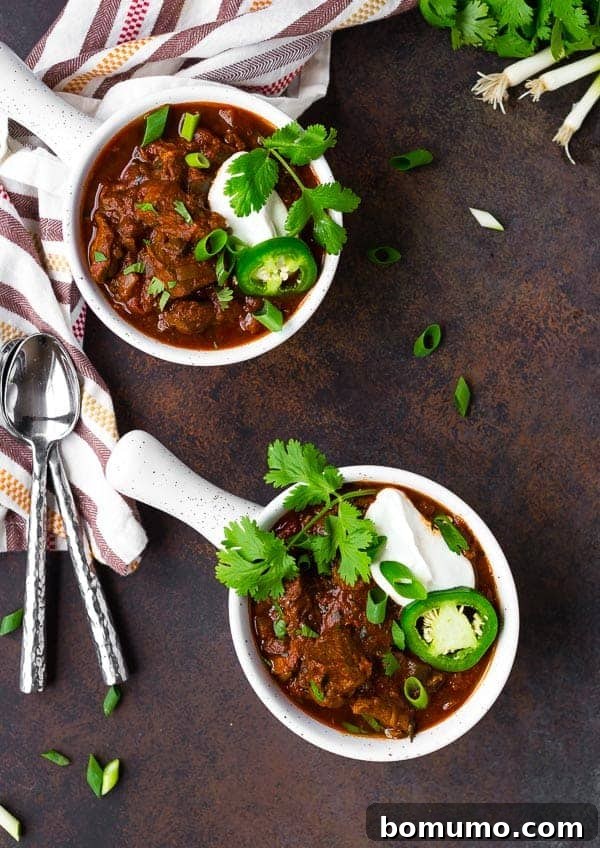 Overhead of chili in a round white bowl with a handle, topped with cilantro, chopped scallions, a slice of pepper, and sour cream.