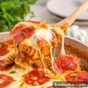 One-Pan Pizza Pasta being scooped from a pan with a wooden spoon, highlighting the cheesy texture.