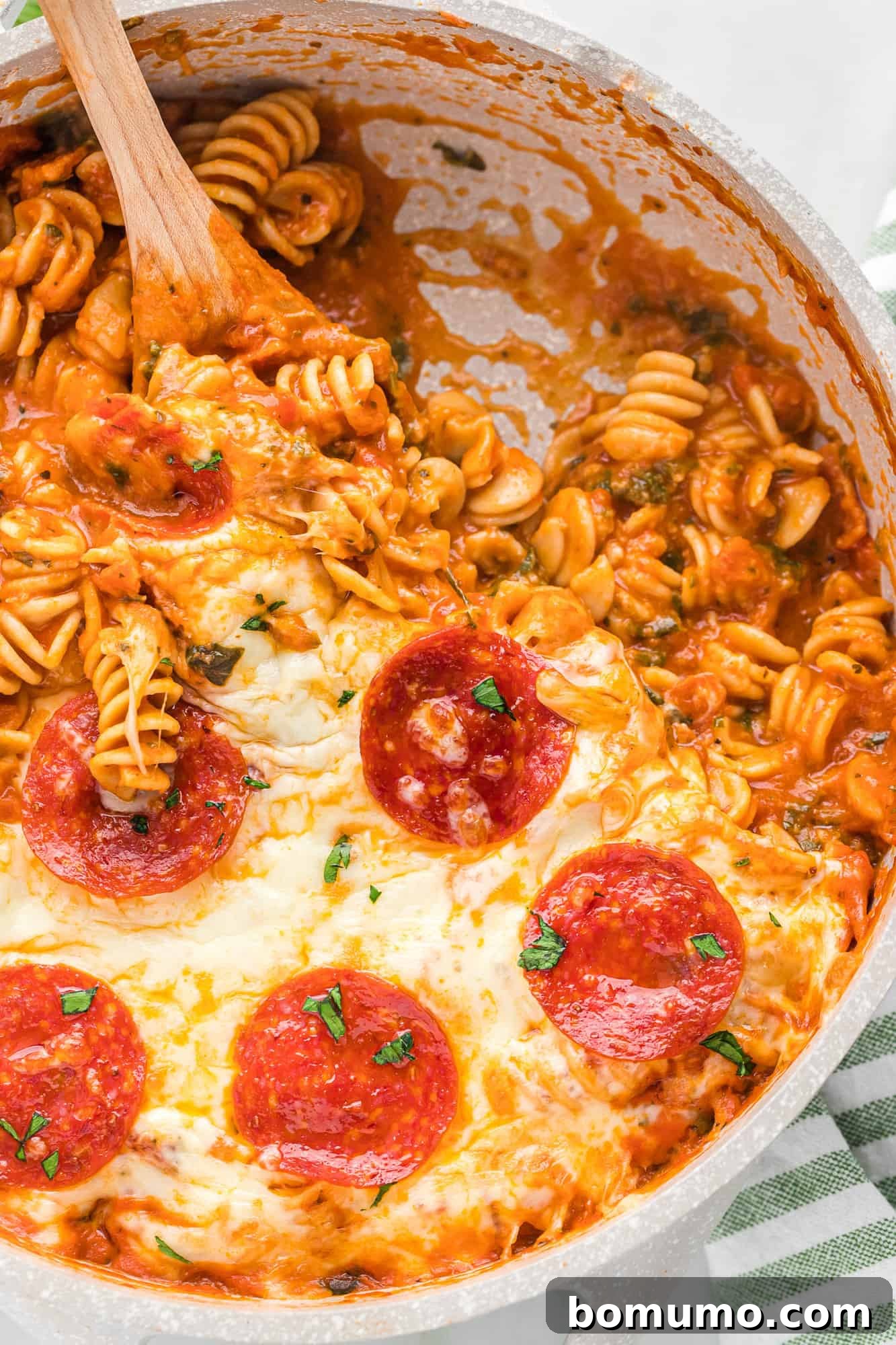 Delicious One-Pan Pizza Pasta with a portion scooped out, showing melted cheese, pasta, and spinach.