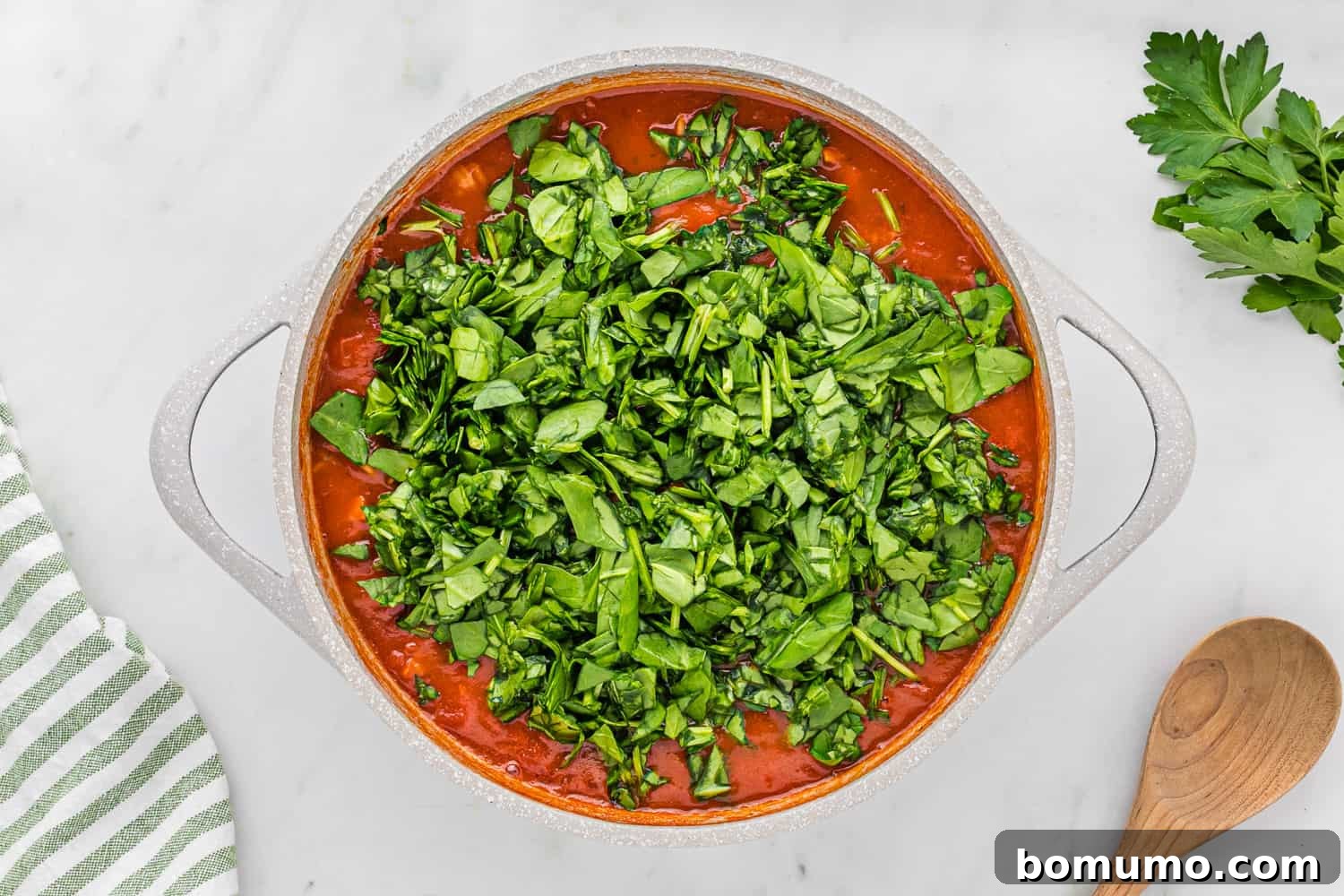 Fresh baby spinach leaves added on top of the cooked pizza pasta and sauce, ready to be wilted.