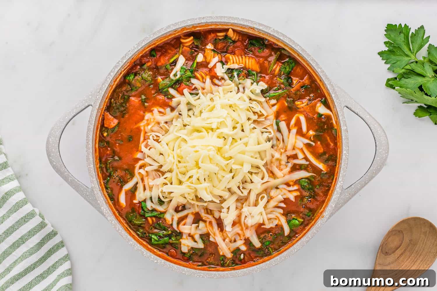 Shredded mozzarella cheese generously sprinkled over the hot pizza pasta, about to be stirred in and melted.