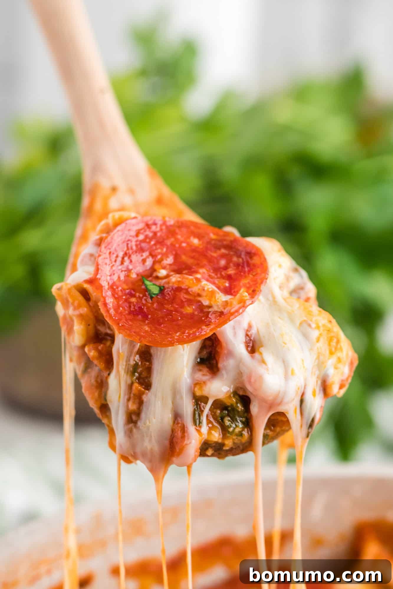 Close-up of One-Pan Pizza Pasta with abundant melted cheese, being served with a wooden spoon.