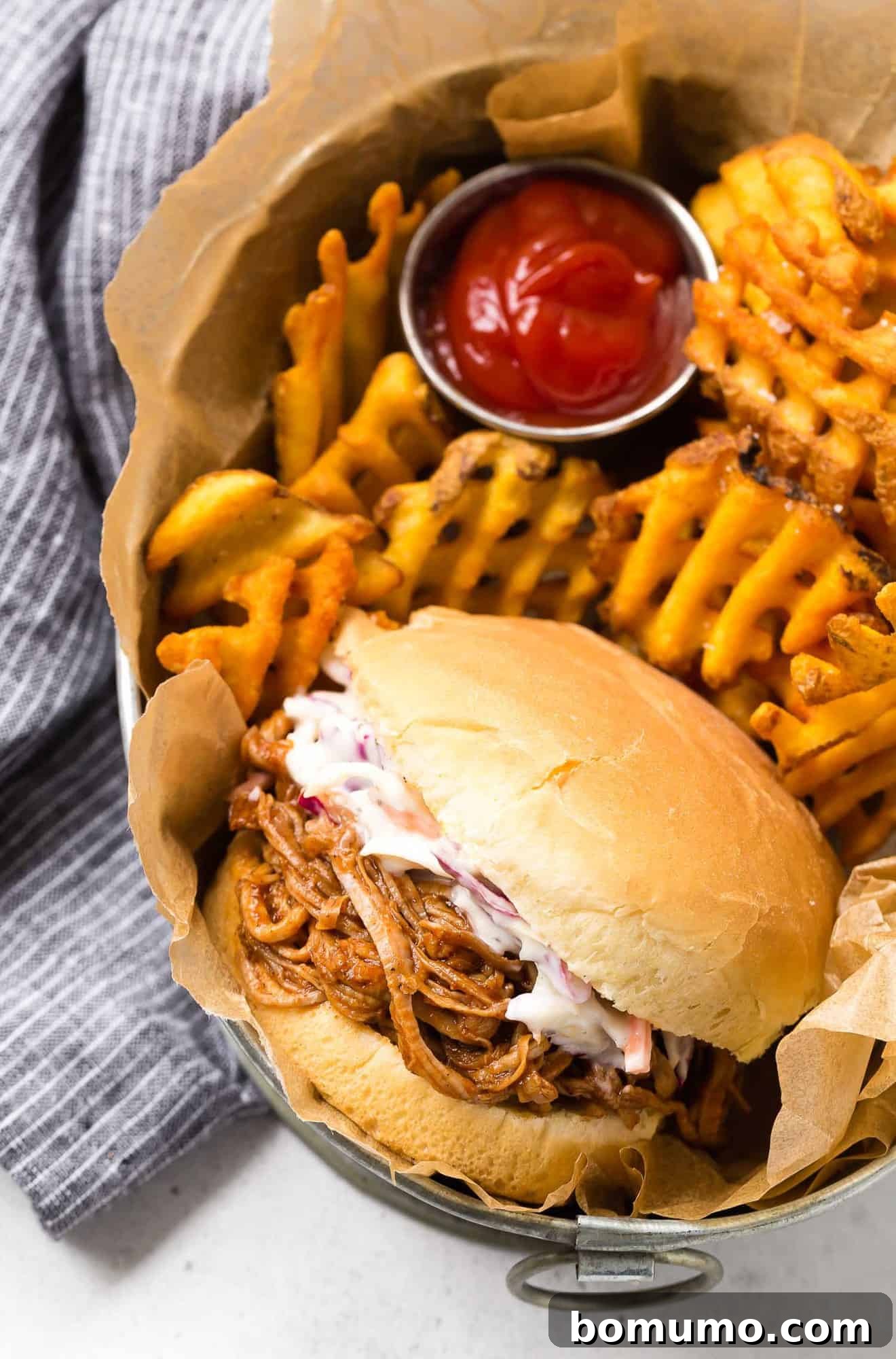 Classic pulled pork sandwich served with crispy waffle fries in a rustic basket, showcasing the perfect texture and deliciousness.