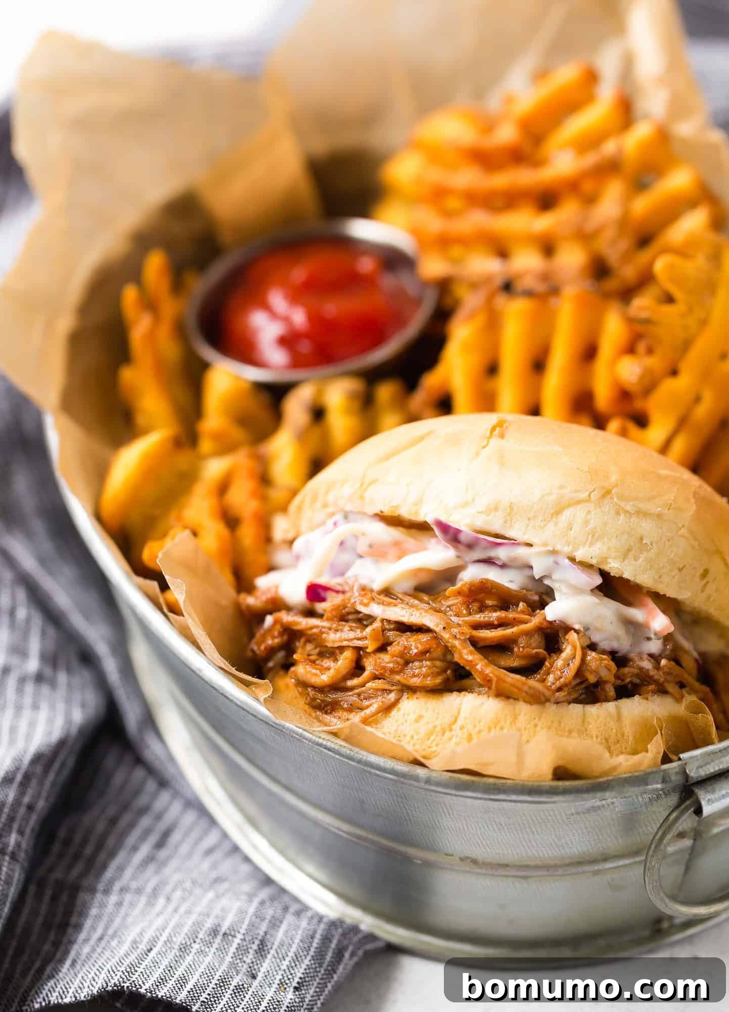 A delectable pulled pork sandwich topped with fresh coleslaw, served in a basket with golden, crispy fries, highlighting a complete and satisfying meal.