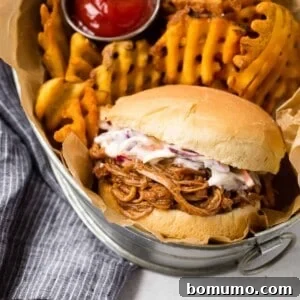 Instant Pot Pulled Pork served on a bun with coleslaw and a side of fries in a basket, emphasizing a full meal presentation.