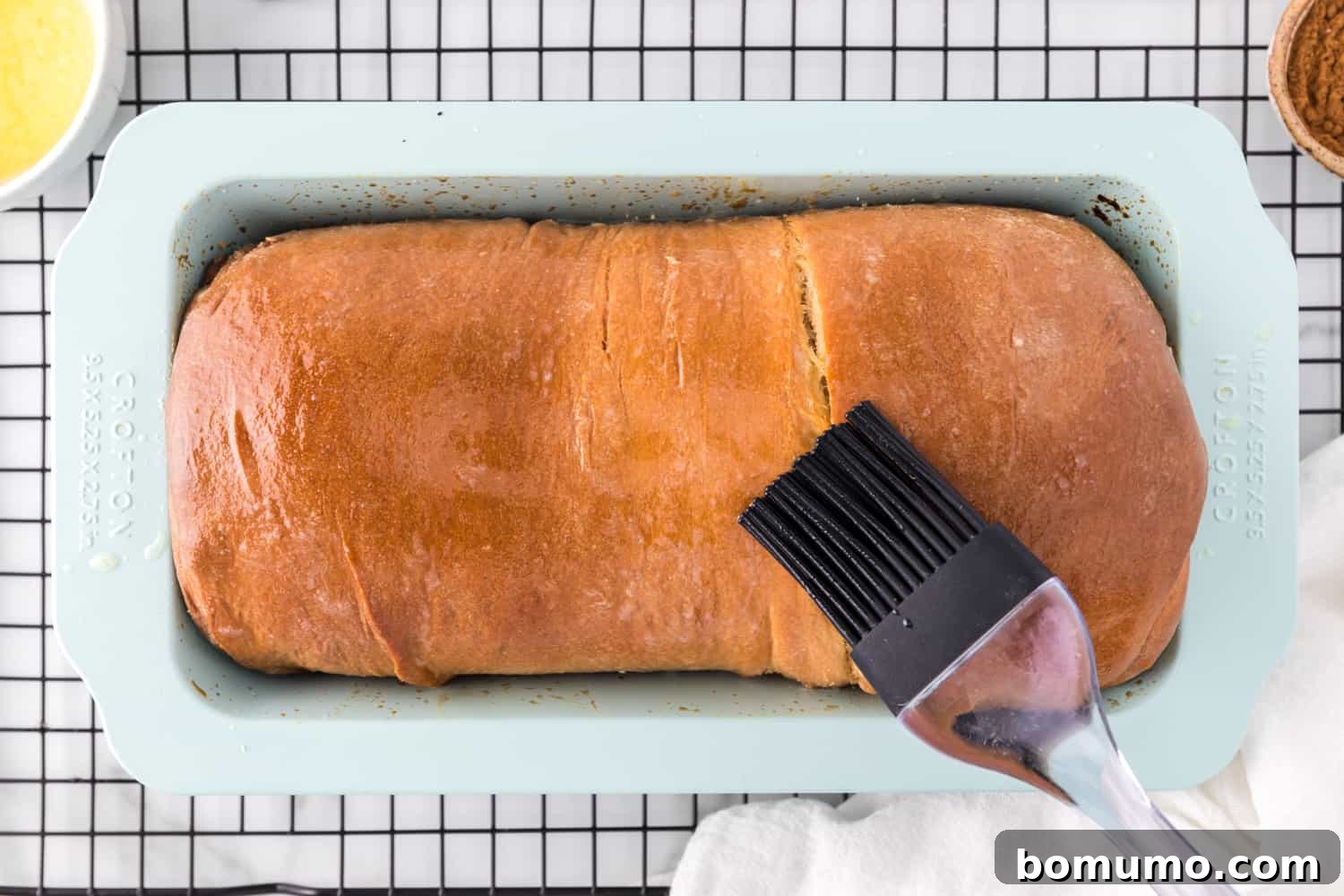 Freshly baked cinnamon swirl bread being brushed with melted butter for a soft crust.