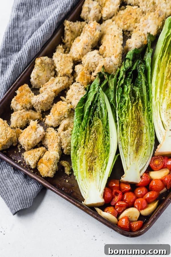 Sheet Pan Roasted Romaine Supper 3 Partial overhead view of a sheet pan laden with ingredients for a sheet pan dinner, including chicken, tomatoes, and garlic.
