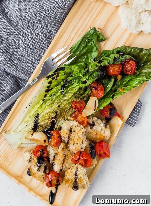 Sheet Pan Roasted Romaine Supper 4 A beautifully plated warm roasted romaine salad featuring golden crispy chicken, sweet roasted tomatoes, and tender roasted garlic, finished with a glossy balsamic glaze. Served on an elegant wooden tray with a fork.