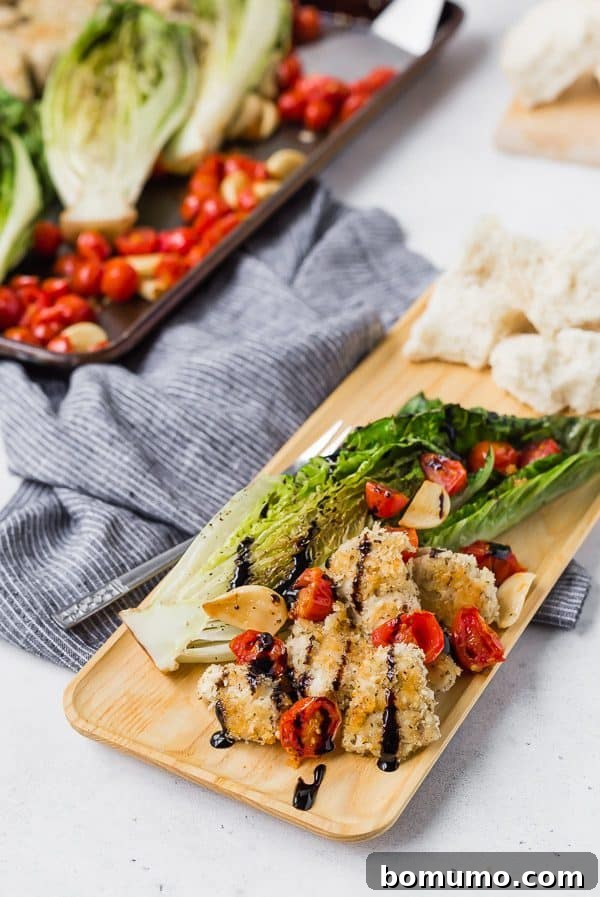 Sheet Pan Roasted Romaine Supper 6 A single serving of the sheet pan dinner, including roasted romaine, crispy chicken, tomatoes, and garlic, elegantly arranged on a rectangular wooden plate.