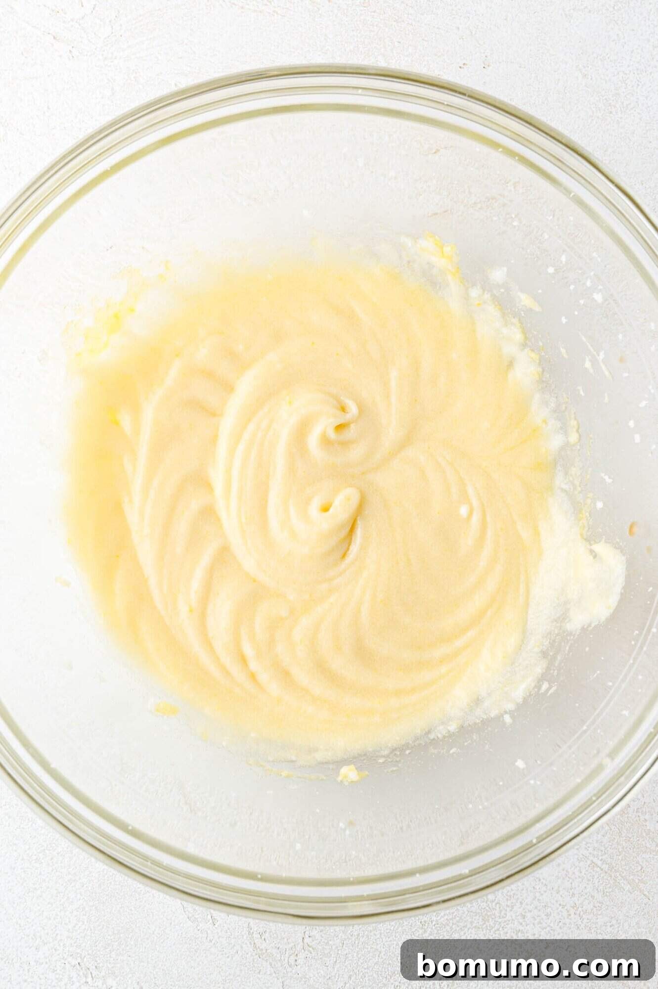 Tangy Rhubarb Cake 11 A clear glass bowl showcasing a smooth, creamy, and pale yellow cake batter mixture, with subtle swirls on the surface, indicating a perfectly blended consistency.