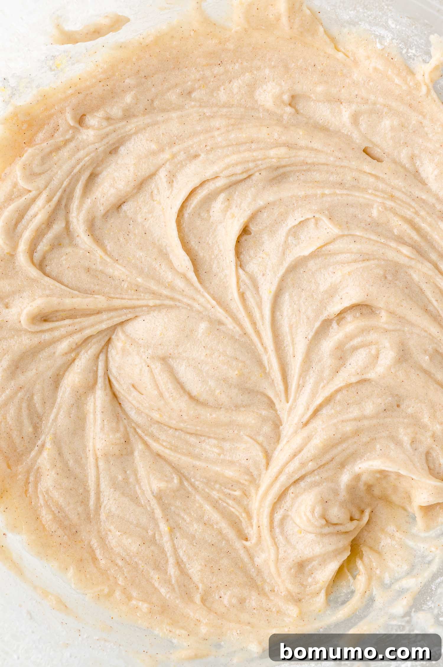 Tangy Rhubarb Cake 14 Close-up of a clear glass bowl filled with a smooth, light brown cake batter, showing visible swirls and a slightly creamy, consistent texture.