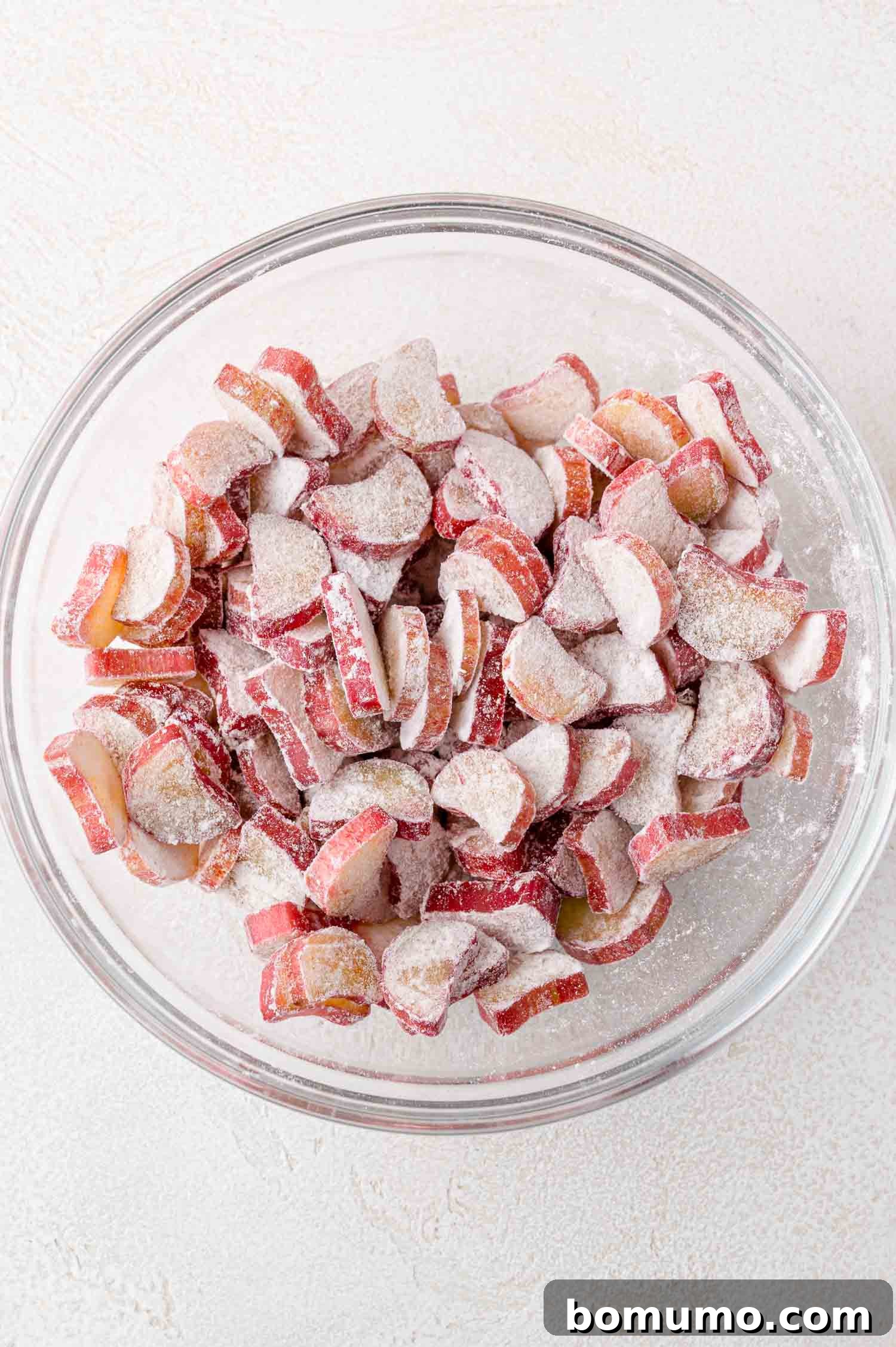 Tangy Rhubarb Cake 8 A transparent glass bowl containing vibrant red sliced rhubarb pieces, lightly coated in a mixture of granulated sugar and flour, awaiting incorporation into the cake batter.