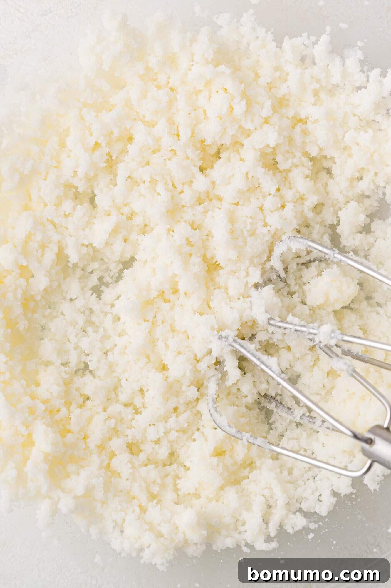 Tangy Rhubarb Cake 9 Electric mixer beaters actively blending creamed butter and sugar in a glass bowl, creating a light, fluffy, and airy texture indicative of proper creaming.