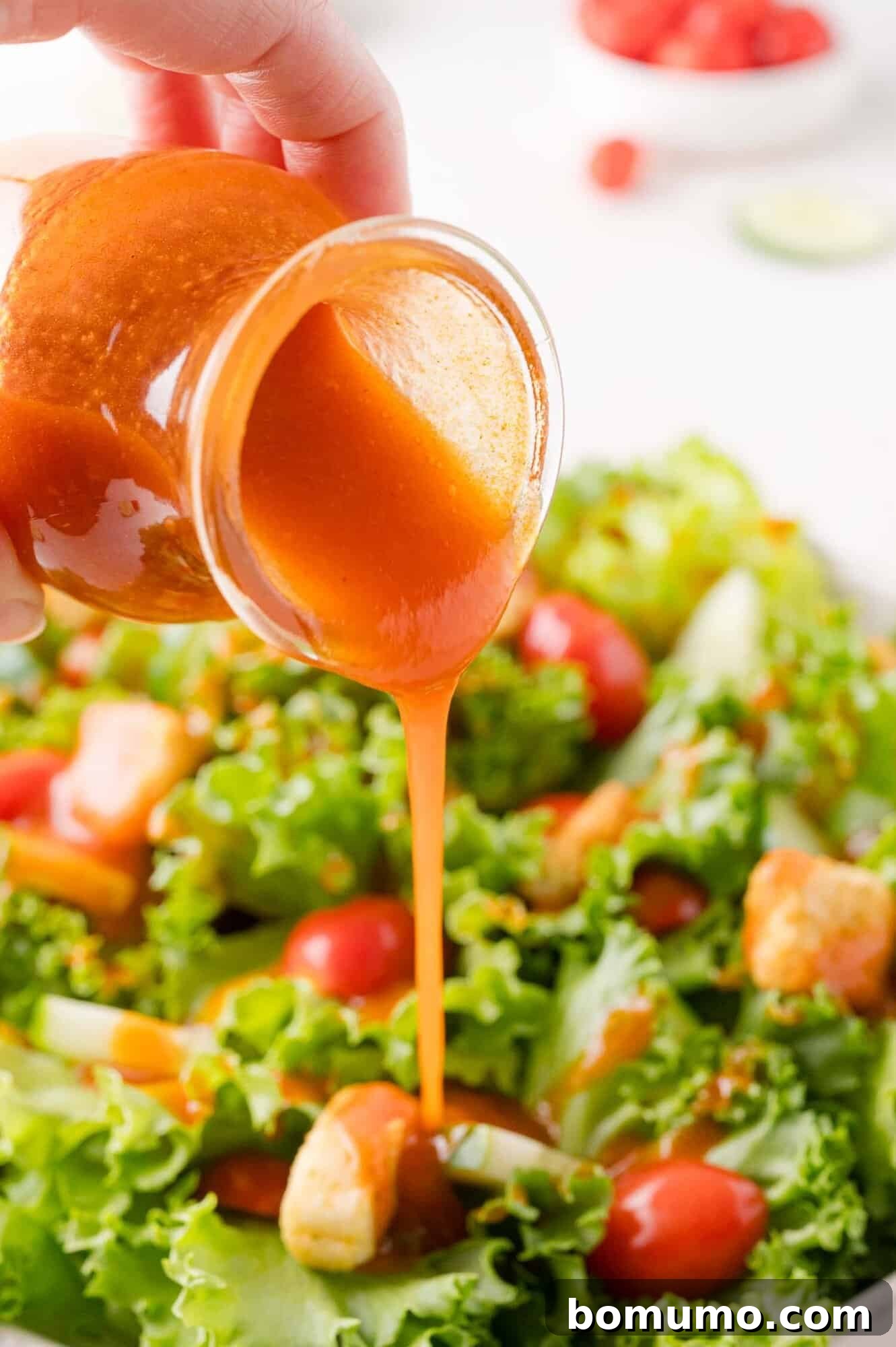 Sunny Tang Dressing 2 Hand pouring orange colored Catalina dressing from a small jar onto a fresh green salad with lettuce, cherry tomatoes, and croutons.