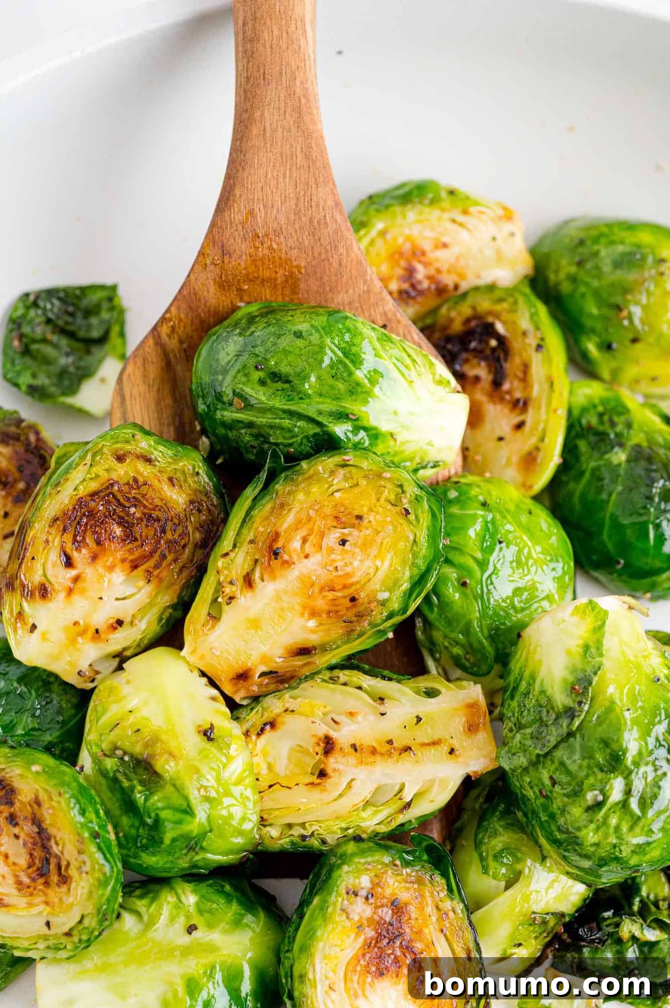 Brussels sprouts in a frying pan with a wooden spoon.