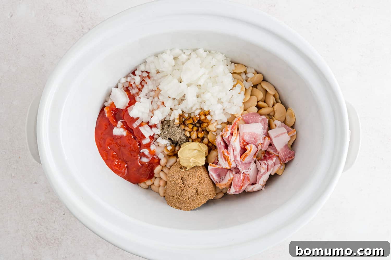 All the uncooked ingredients for baked beans, including beans, bacon, and sauce components, nestled together in a slow cooker before stirring.