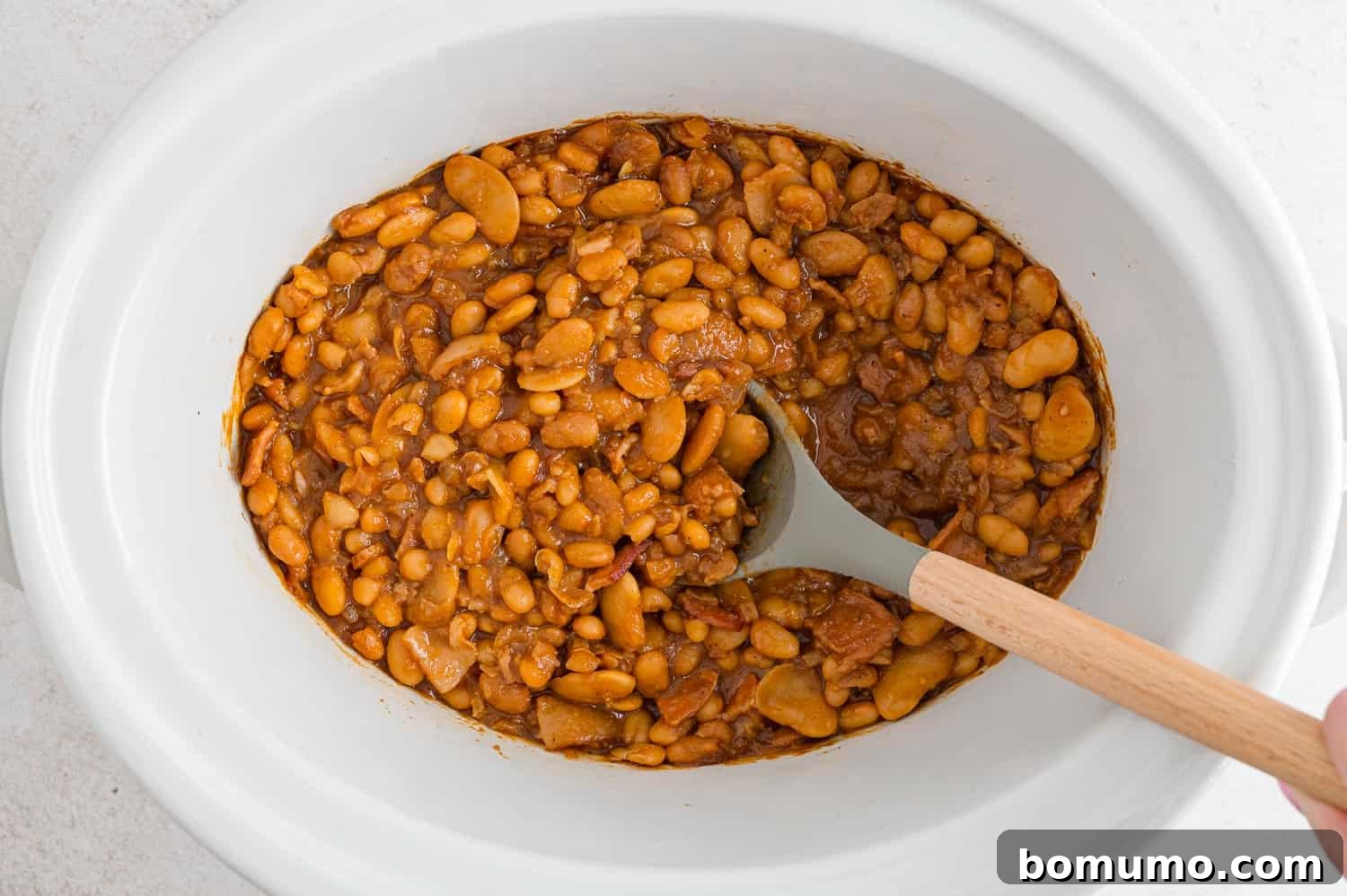 Perfectly cooked, bubbling crock pot baked beans simmering in a slow cooker, ready to serve.