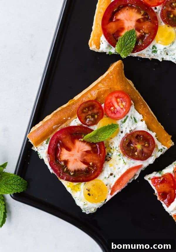 A close-up side view of the freshly baked tomato tart, highlighting the golden-brown, puffed edges of the pastry, the rich texture of the ricotta filling, and the glistening slices of ripe tomatoes, garnished with fresh herbs.