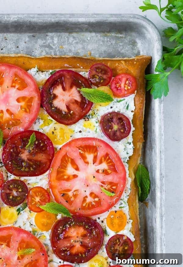 A visually appealing shot of the completed fresh tomato tart with herbed ricotta, seen from a slight angle. The golden crust is visible, along with the generous layer of creamy ricotta and thinly sliced tomatoes, adorned with fresh mint leaves.