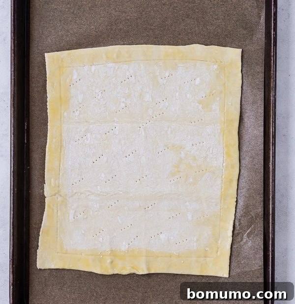 An image demonstrating the preparation of puff pastry for a tart. The pastry sheet is scored around the edges to create a border and pricked in the center with a fork to prevent excessive rising during baking.