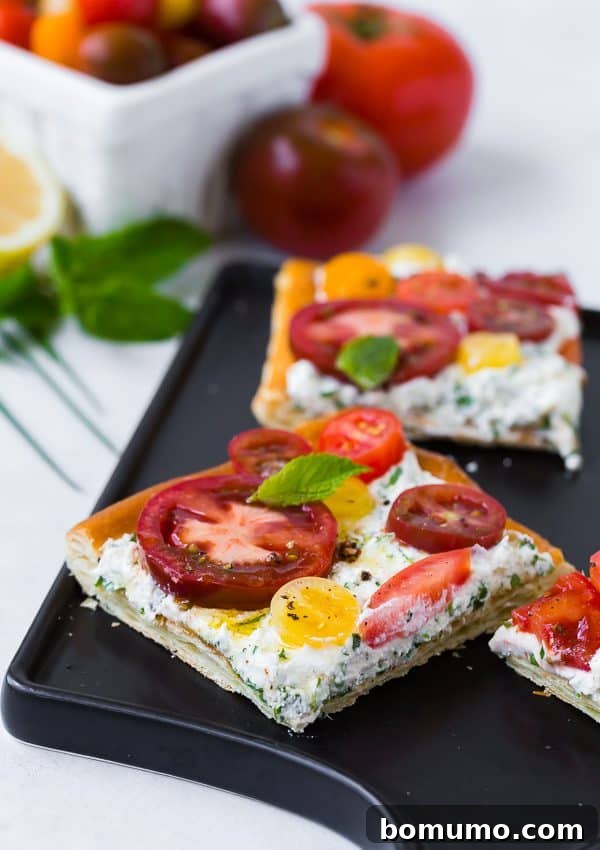 The finished fresh tomato tart with herbed ricotta, beautifully presented and ready to serve. The vibrant red and yellow tomatoes are arranged on a white ricotta base, surrounded by a puffed, golden pastry crust, and garnished with fresh green herbs.