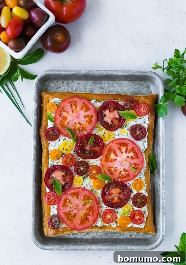 A final close-up shot of the fresh tomato tart with herbed ricotta, showing a slice cut out, revealing the layers of flaky pastry, creamy filling, and colorful tomatoes. It's ready to be served and enjoyed.
