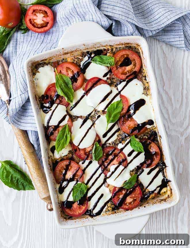 Overhead view of chicken Caprese in a white rectangular baking dish, garnished with fresh tomatoes, basil, mozzarella, and drizzled with balsamic glaze.